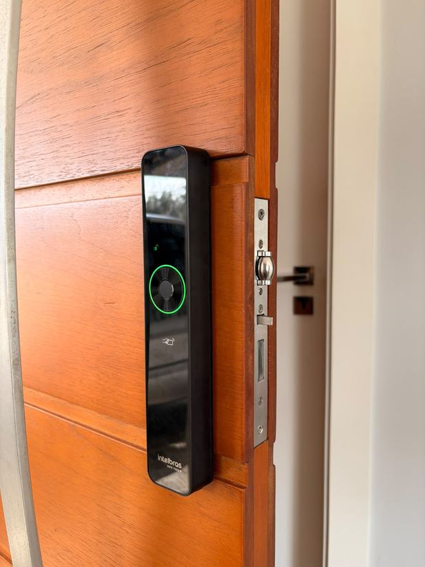 Fechadura digital Intelbras instalada em porta de madeira maciça, anel indicador aceso em verde