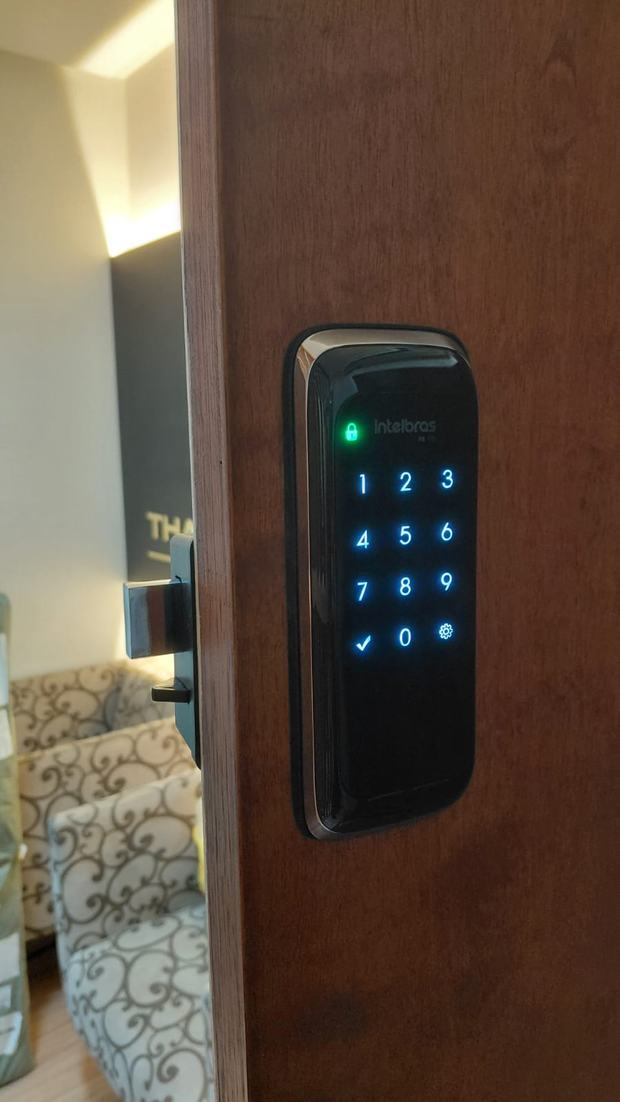 Fechadura digital Intelbras com teclado iluminado em azul, em porta de madeira escura