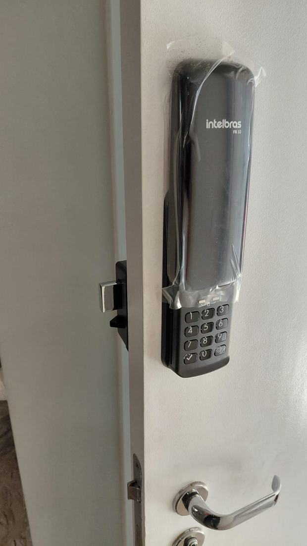 Fechadura digital Intelbras prateada instalada em porta clara